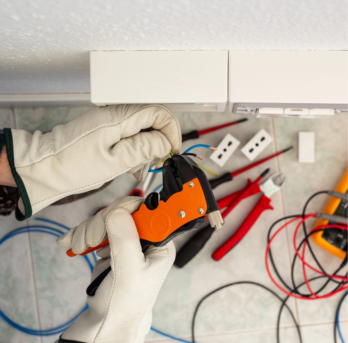 Hands using an orange multimeter for electrical testing.